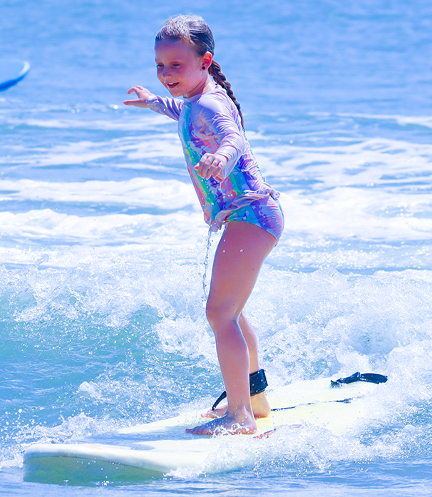Young girl surfing on a wave in a colorful swimsuit.