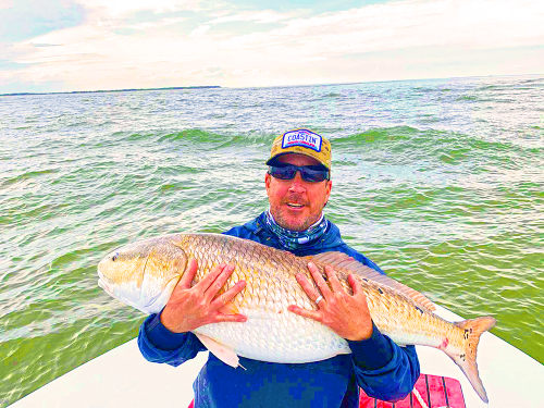 Man holding a large fish on a boat with water in the background
